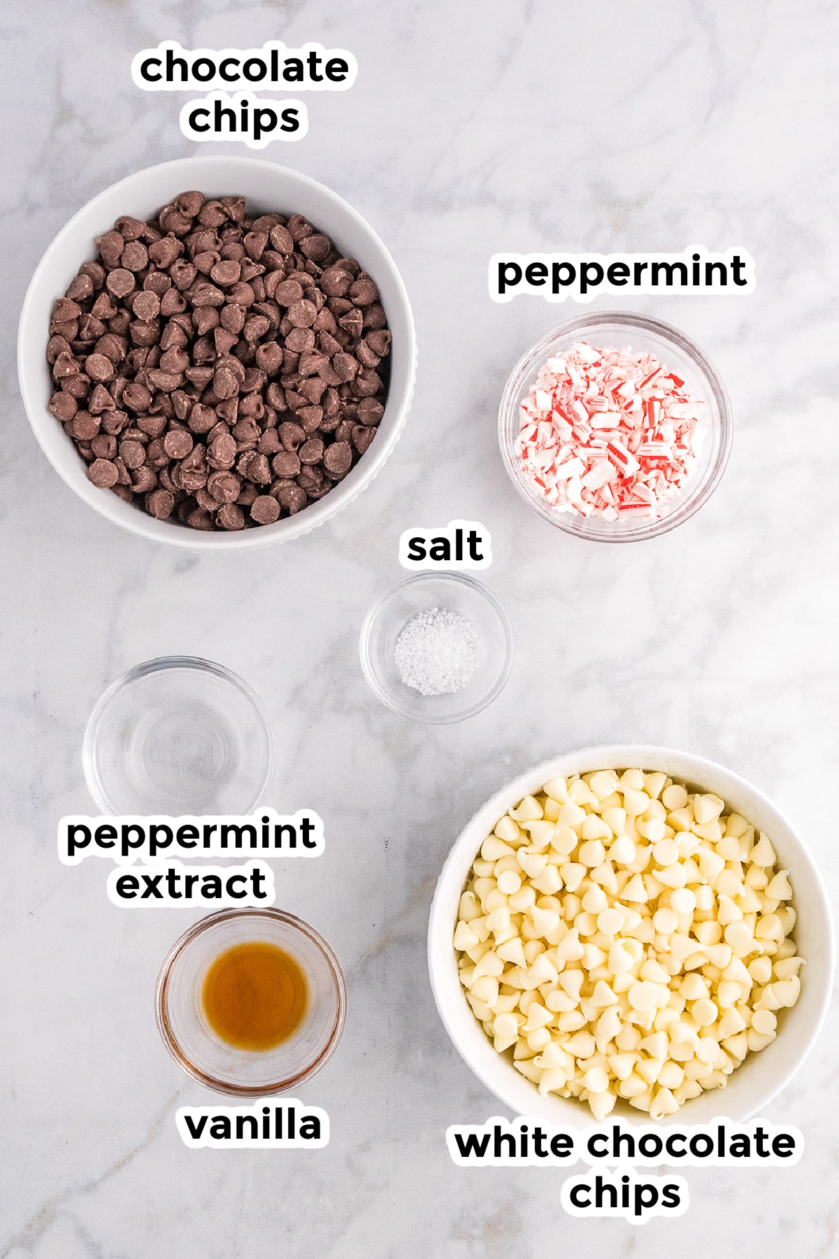 Ingredients for peppermint bark in bowls on a counter with text labels from overhead.
