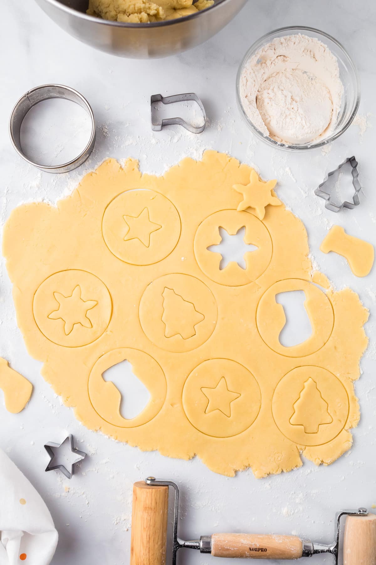 Christmas sugar cookie dough being cut into round circles with the centers of each circle being cut into different holiday shapes.