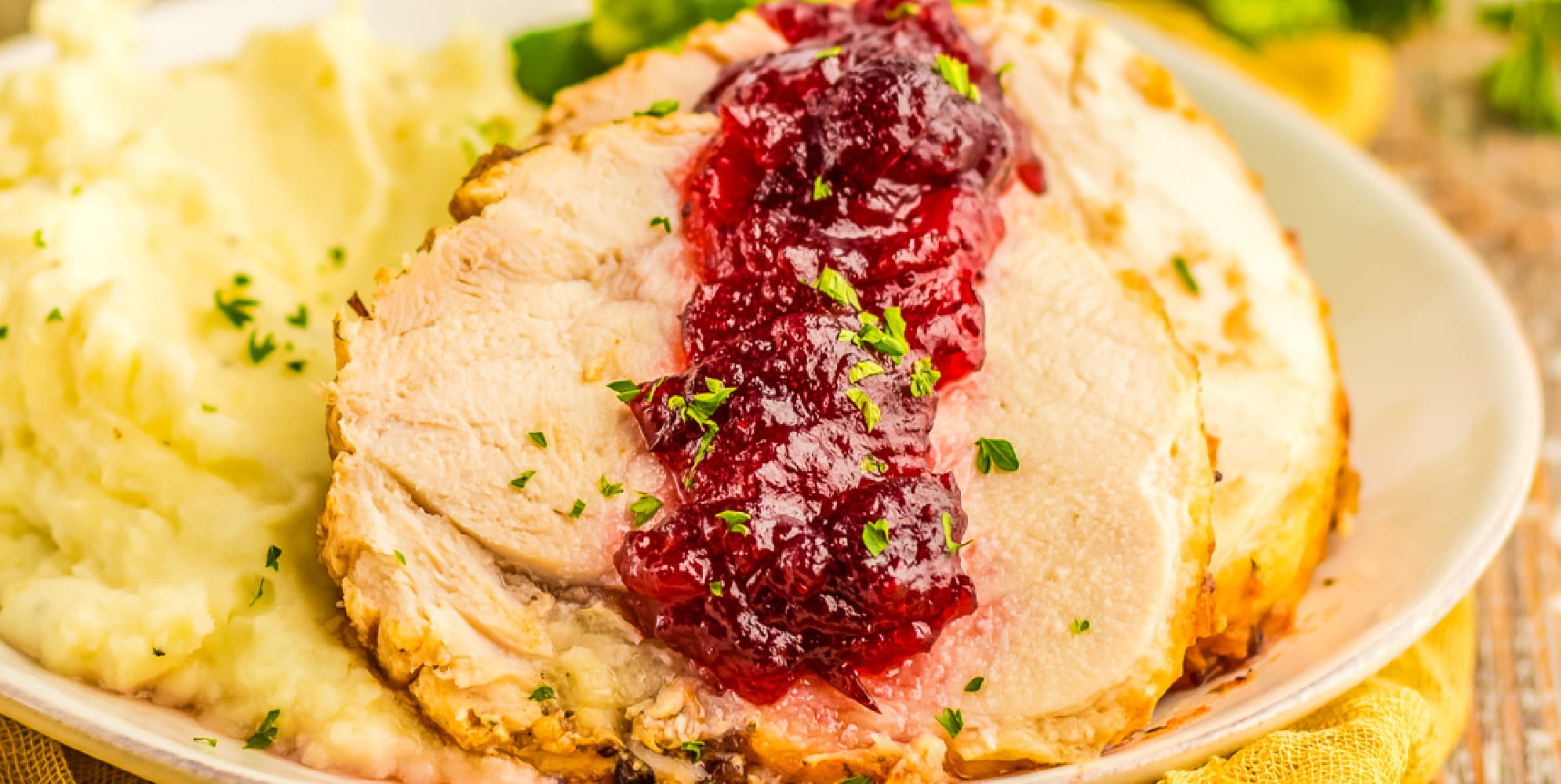 Wide view of sliced turkey with cranberry sauce and mashed potatoes on a plate.