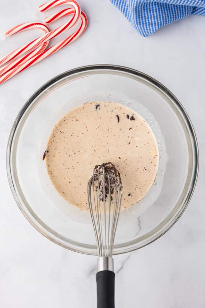 A glass bowl with a whisk mixing warm cream and chocolate together.