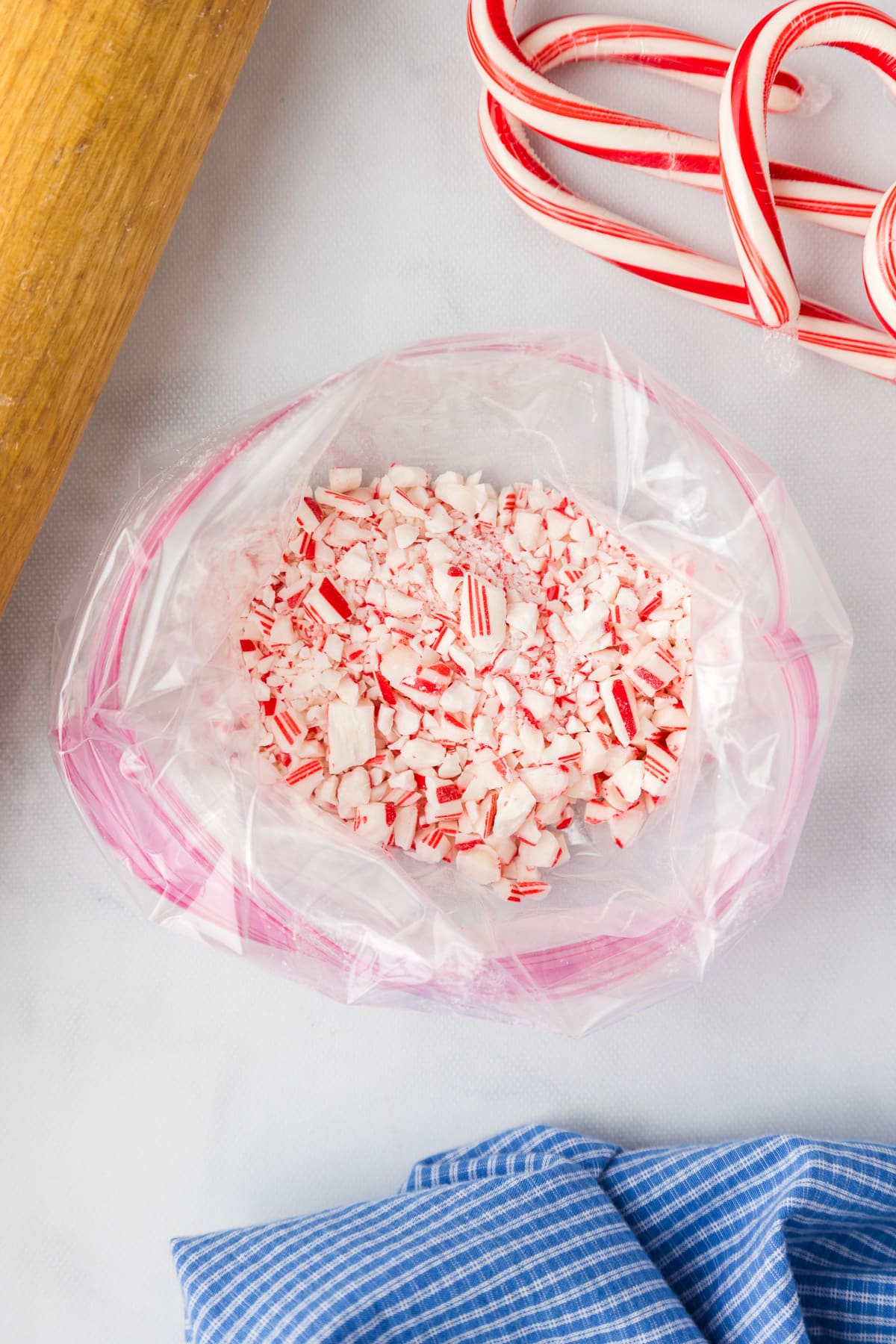 Candy canes in a plastic bag next to a rolling pin.