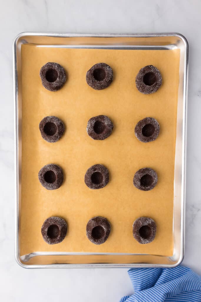 Unbaked chocolate peppermint thumbprint cookies on a baking sheet with holes pressed into the center of each cookie.