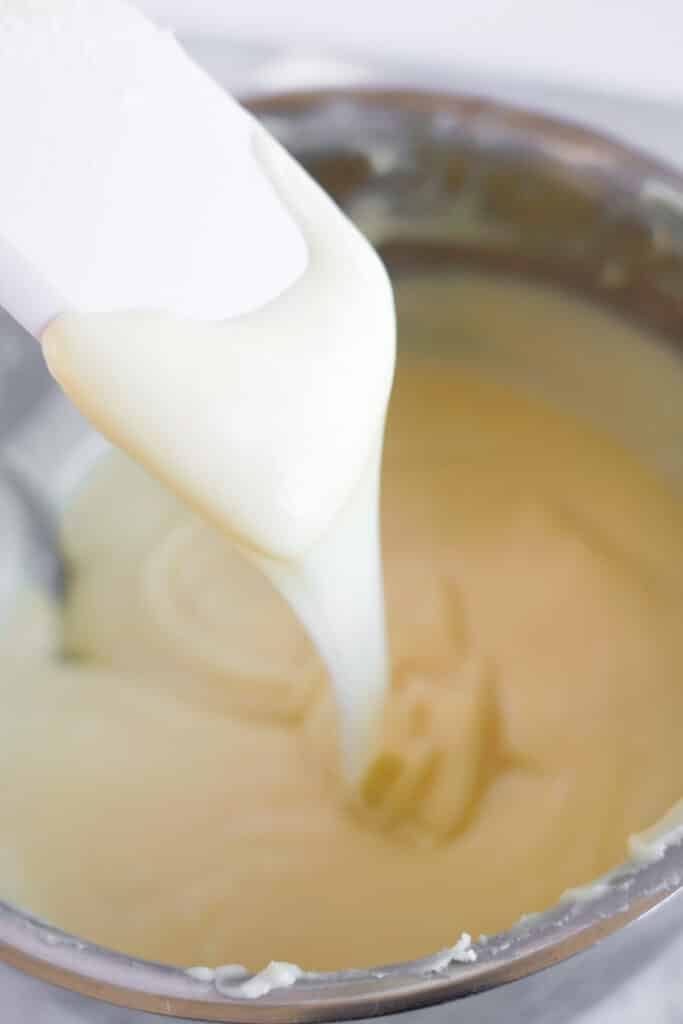 A spatula pulling smooth melted vanilla fudge batter out of a pot.