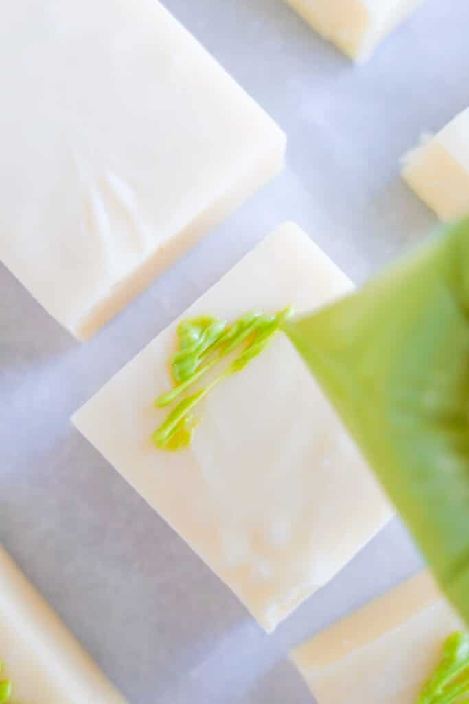 squares of vanilla fudge up close being decorated with green chocolate trees.