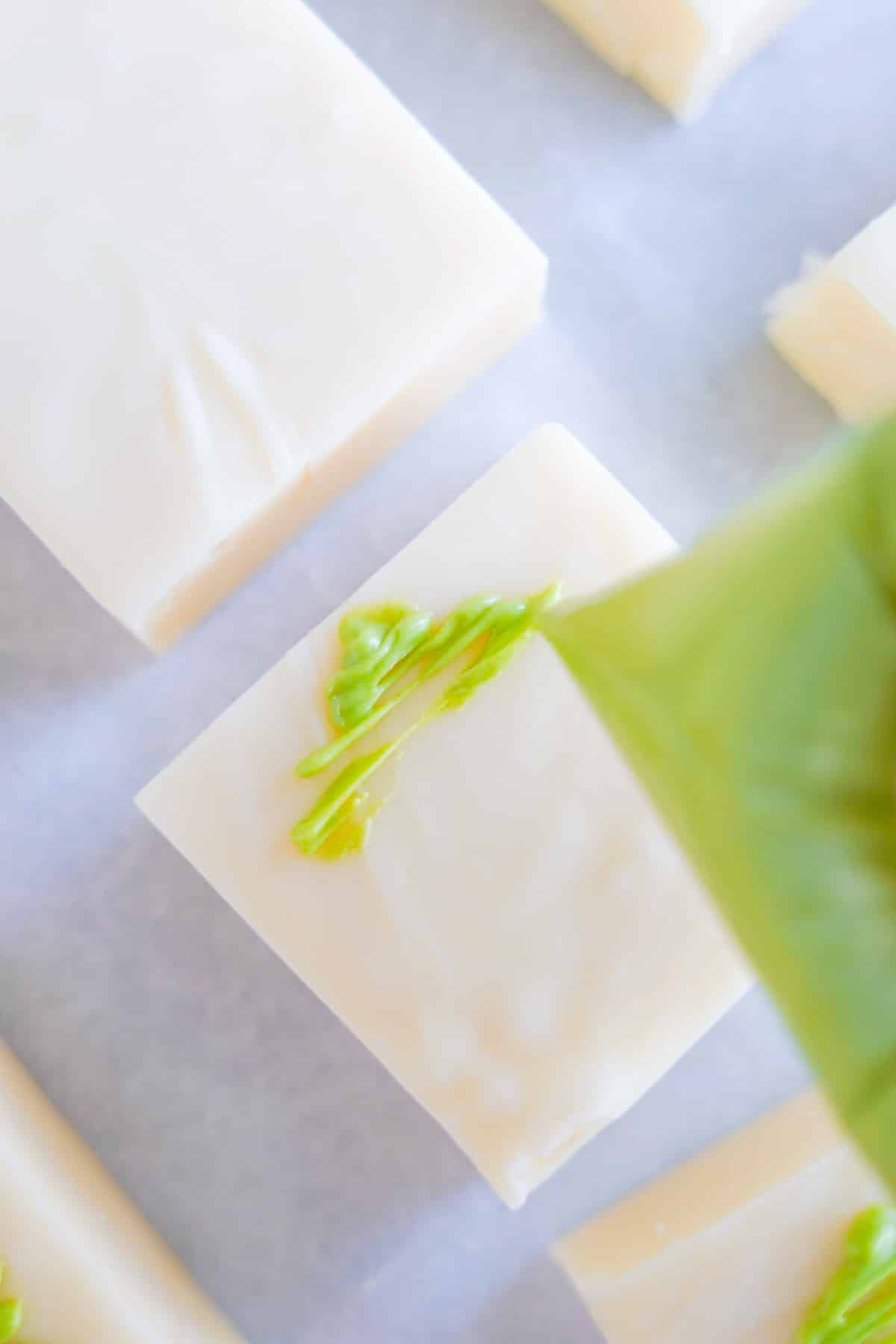 squares of vanilla fudge up close being decorated with green chocolate trees.