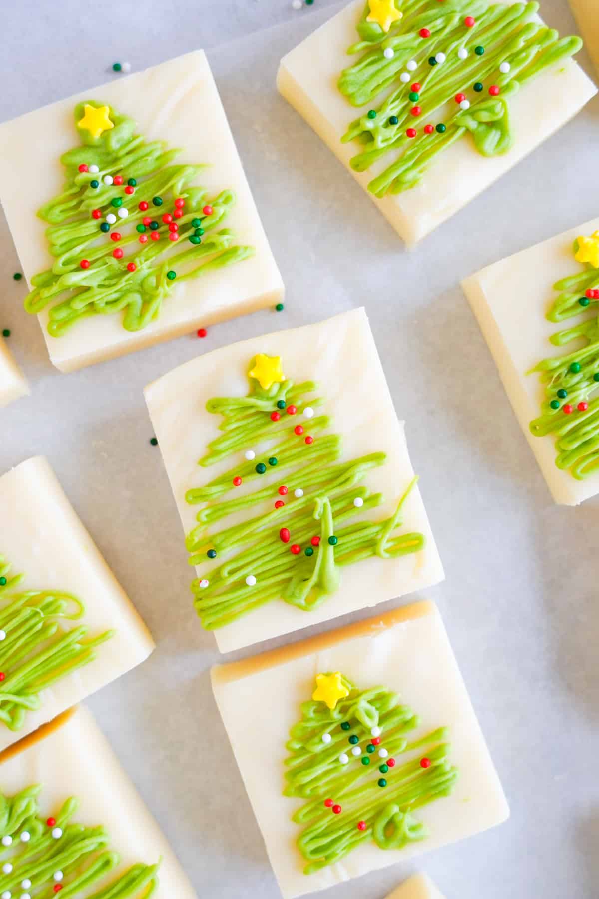 Pieces of vanilla fudge decorated with green chocolate Christmas trees and sprinkles.