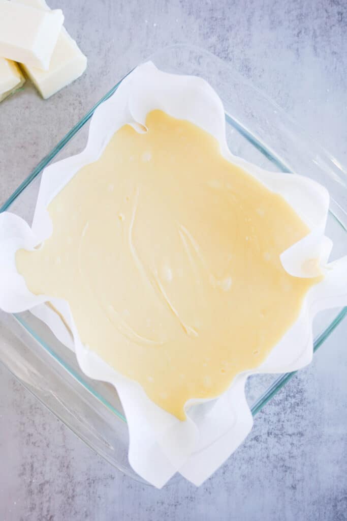 A square baking dish lined with parchment paper full of vanilla fudge.
