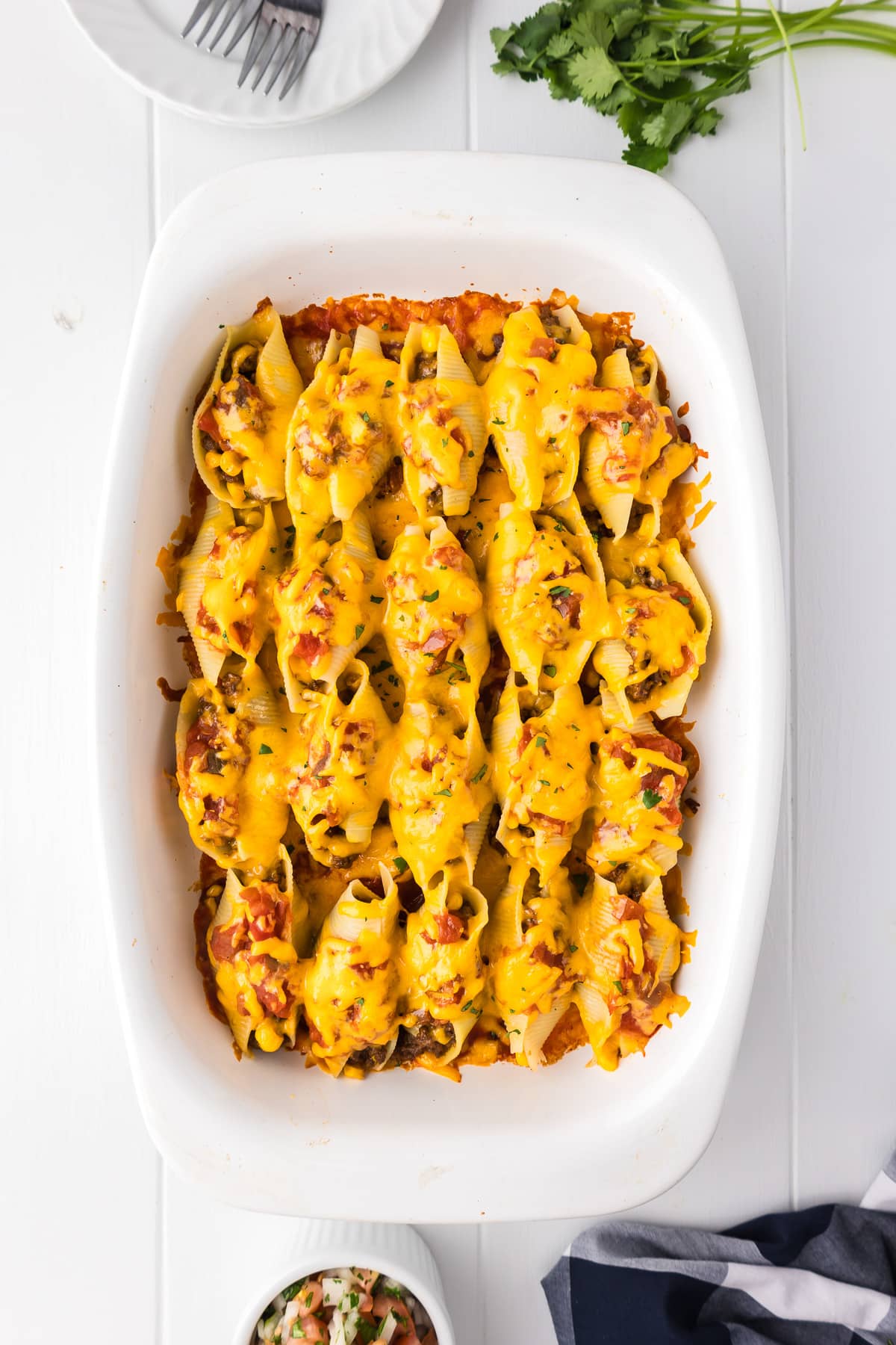 Taco stuffed shells lined up in a casserole dish with melted cheese on top.