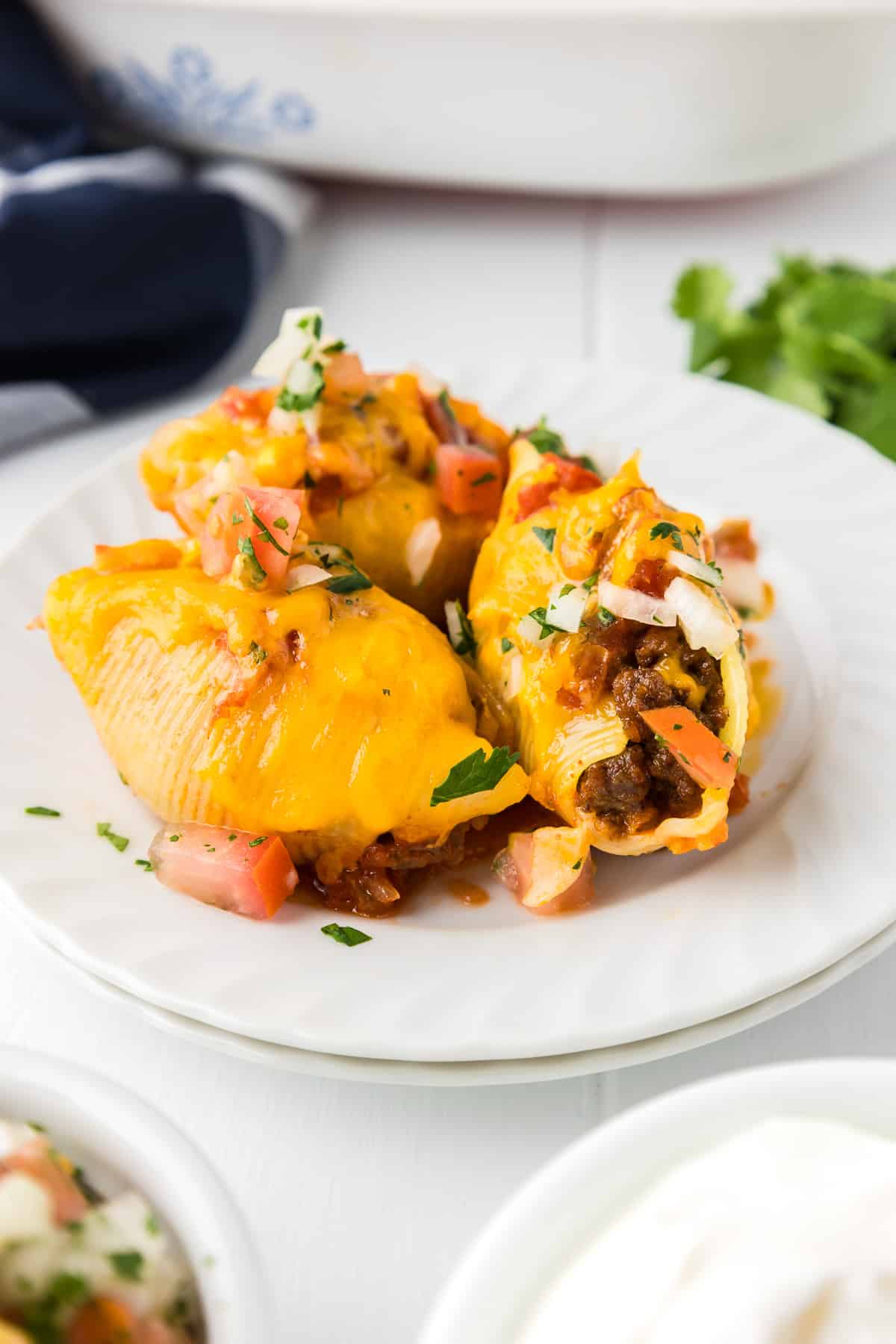 Three Mexican stuffed shells on a plate with salsa and one shell with a bite missing.