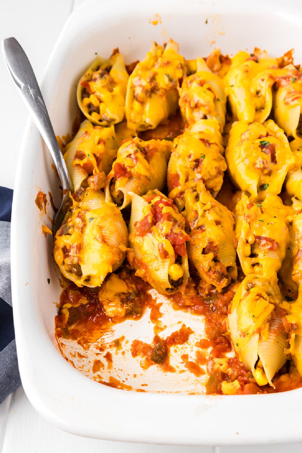 Mexican stuffed shells in a baking dish being scooped by a spoon with a few shells missing from the pan.