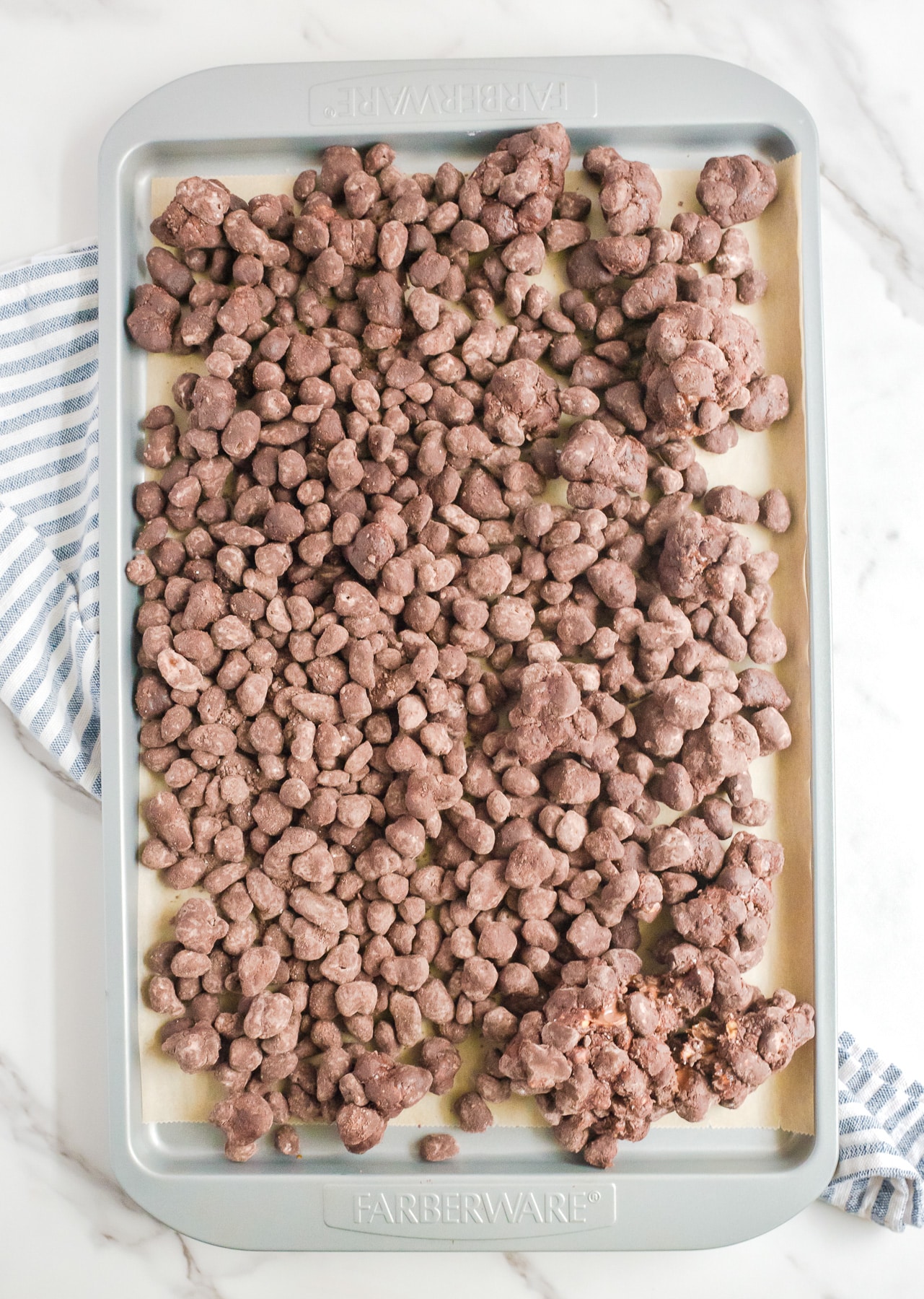 Reindeer poop chocolate snack mix spread out on a pan covered in parchment paper.