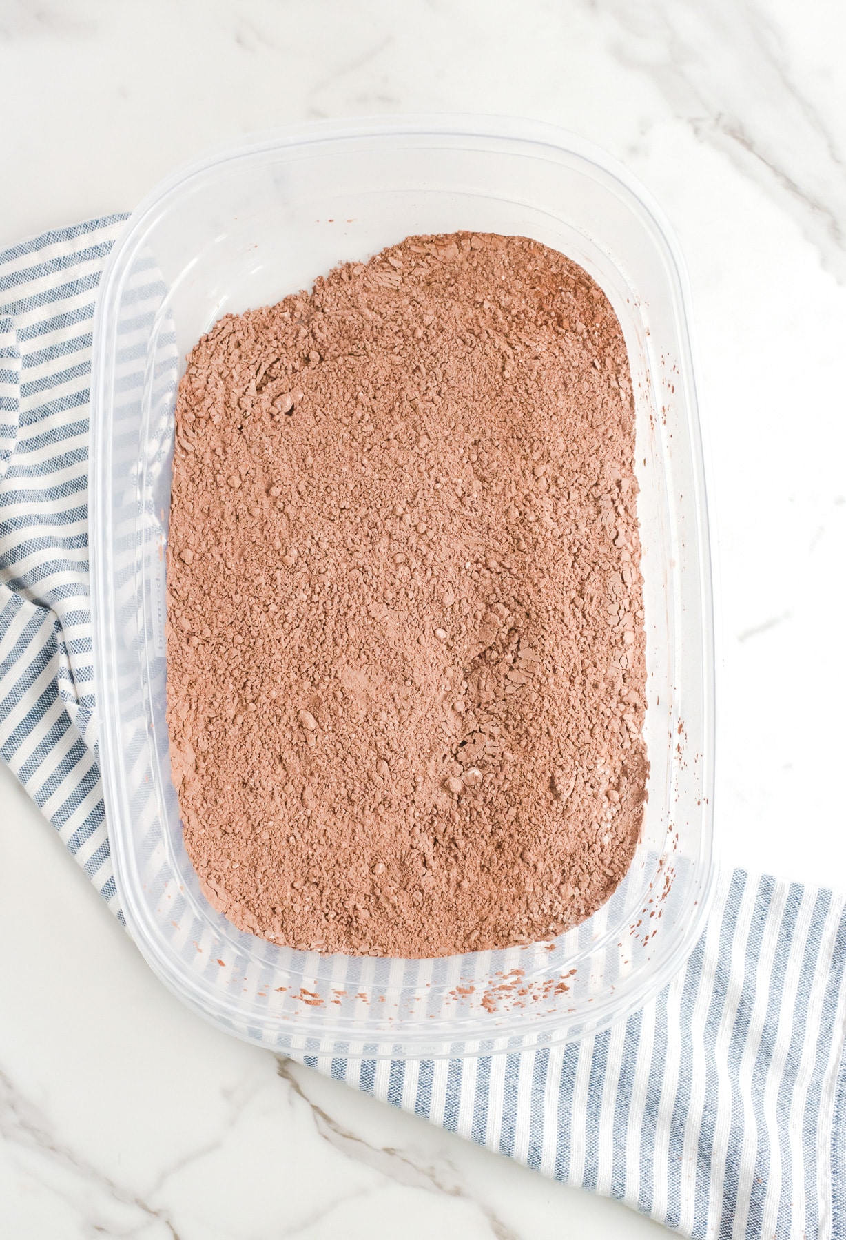 A plastic container with chocolate and powdered sugar mixed together in it.
