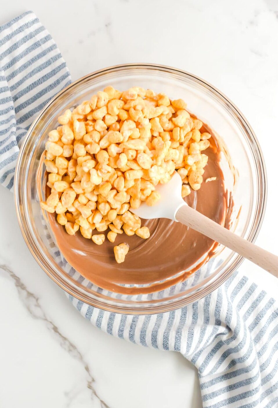 Corn Pops being added to melted chocolate in a large bowl being mixed by a spatula.