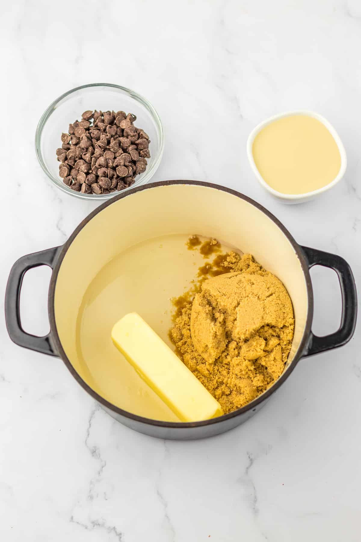 Butter, brown sugar and corn syrup in a large pot with chocolate chips and sweetened condensed milk nearby.
