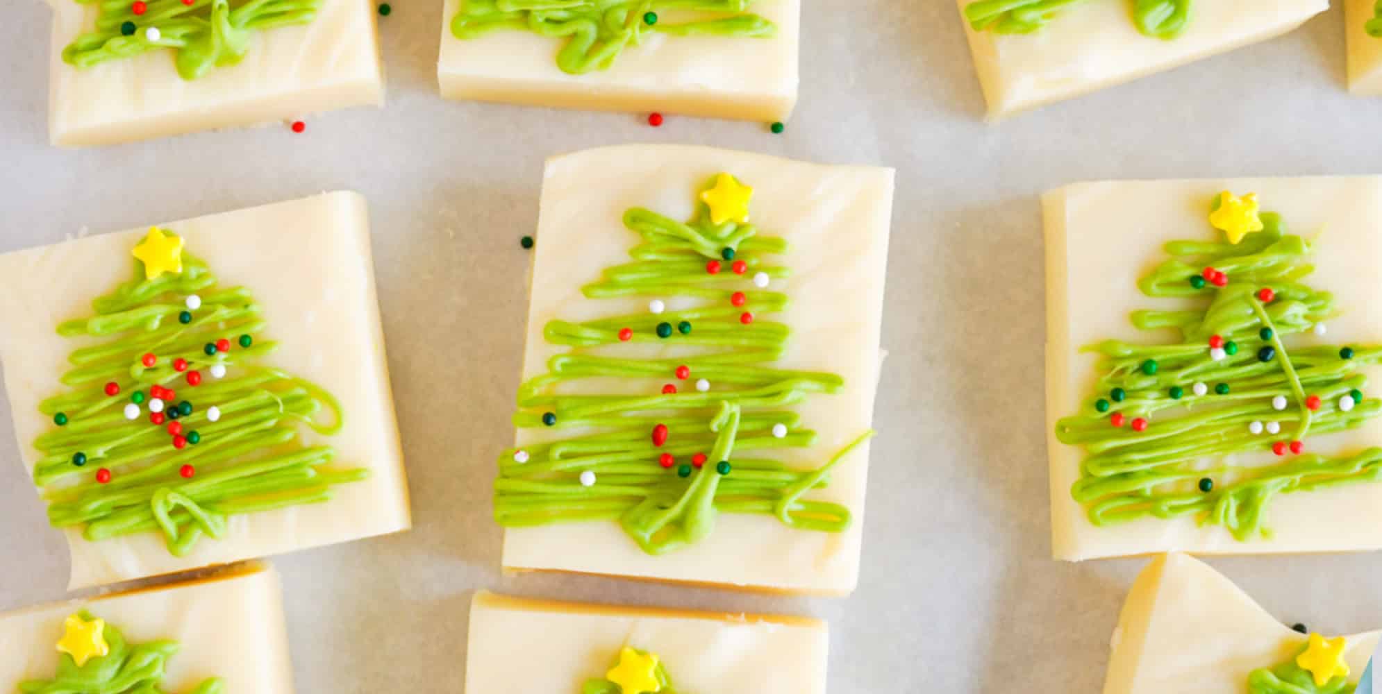 Wide view of pieces of vanilla fudge decorated with green chocolate Christmas trees and sprinkles.