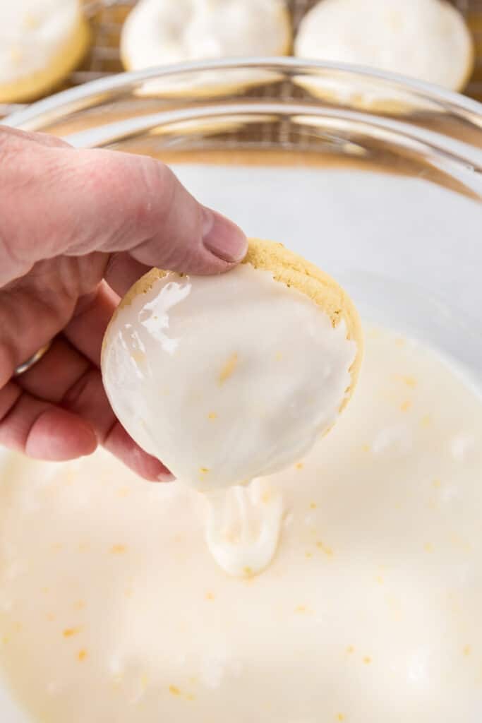 A hand dipping a cookie into a bowl of lemon glaze.