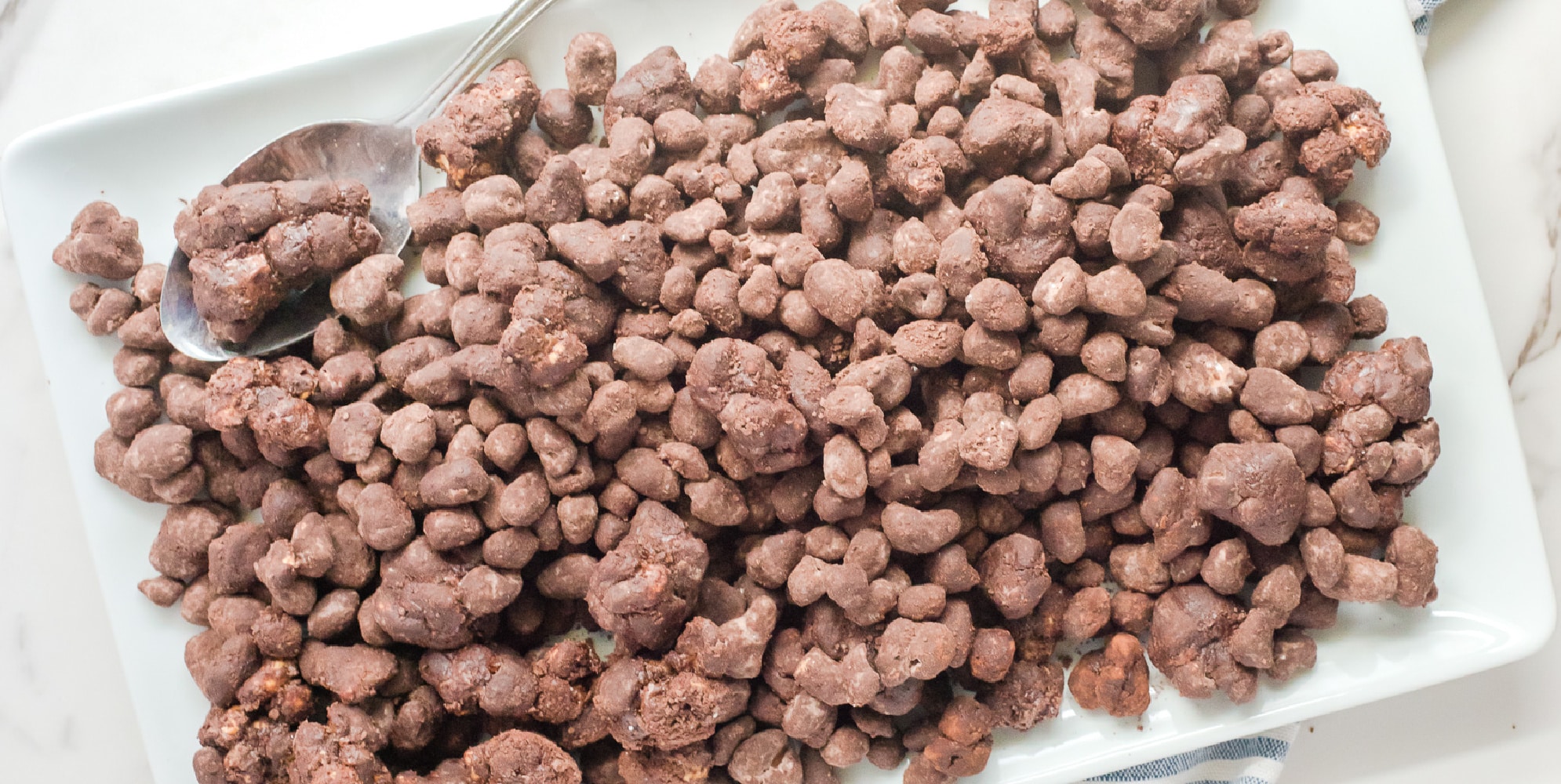 A platter full of chocolate reindeer poop snack mix with a spoon on it.