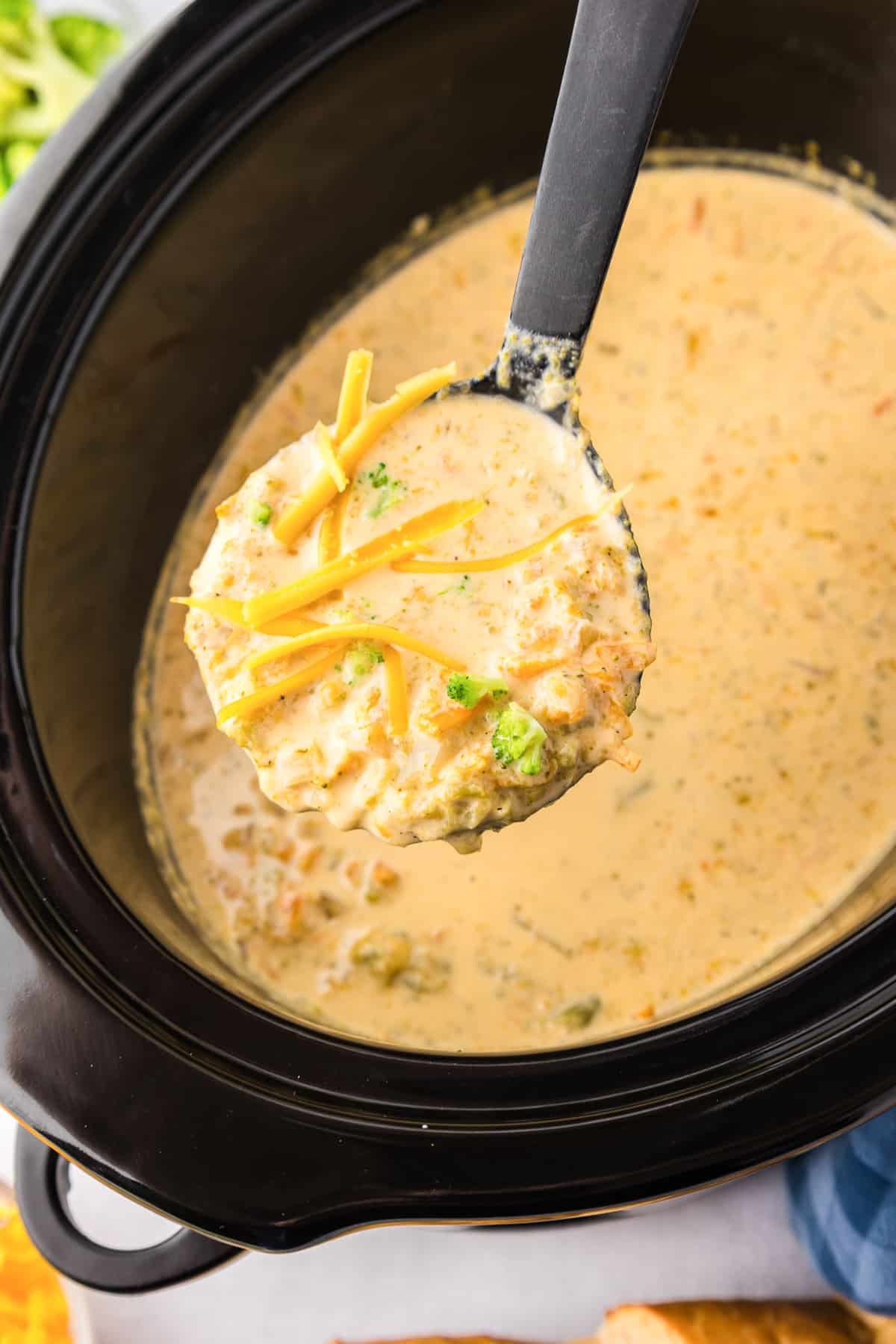 A ladle lifting a scoop of broccoli cheese soup from a slow cooker.