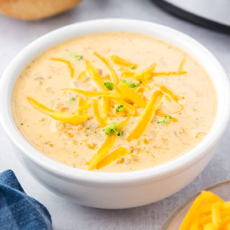 Cheesy broccoli soup in a white bowl topped with extra shredded cheese.