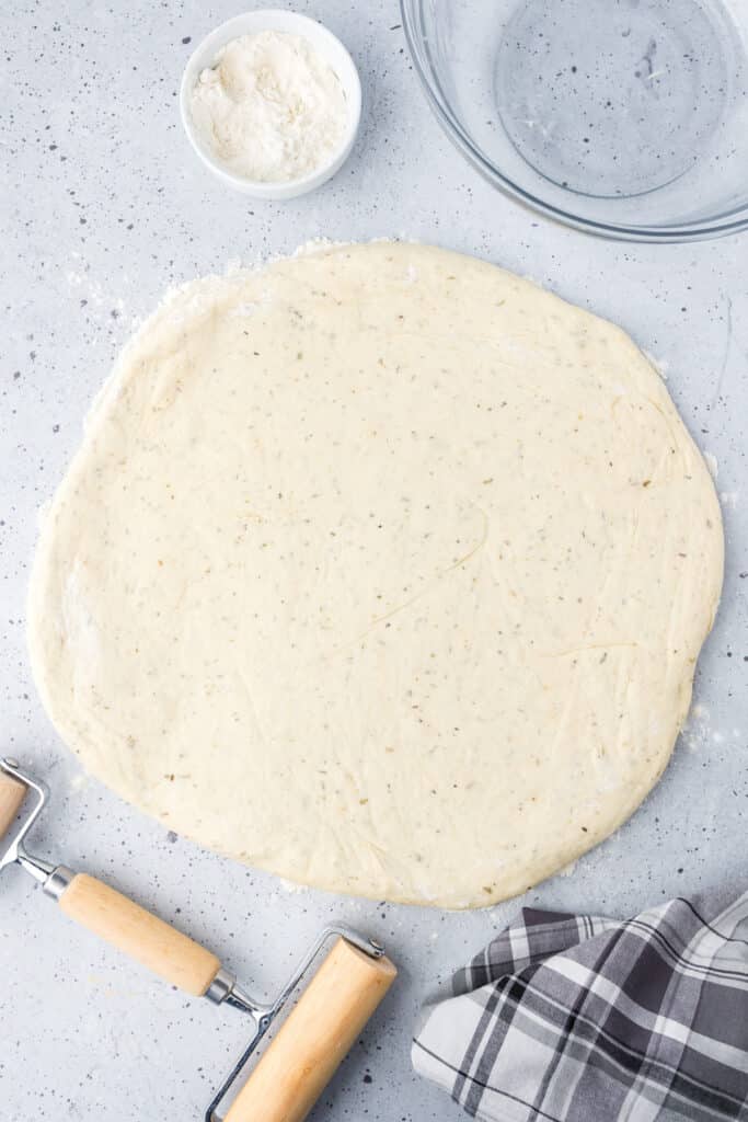 A pizza dough on a counter after rolling with a rolling pin.