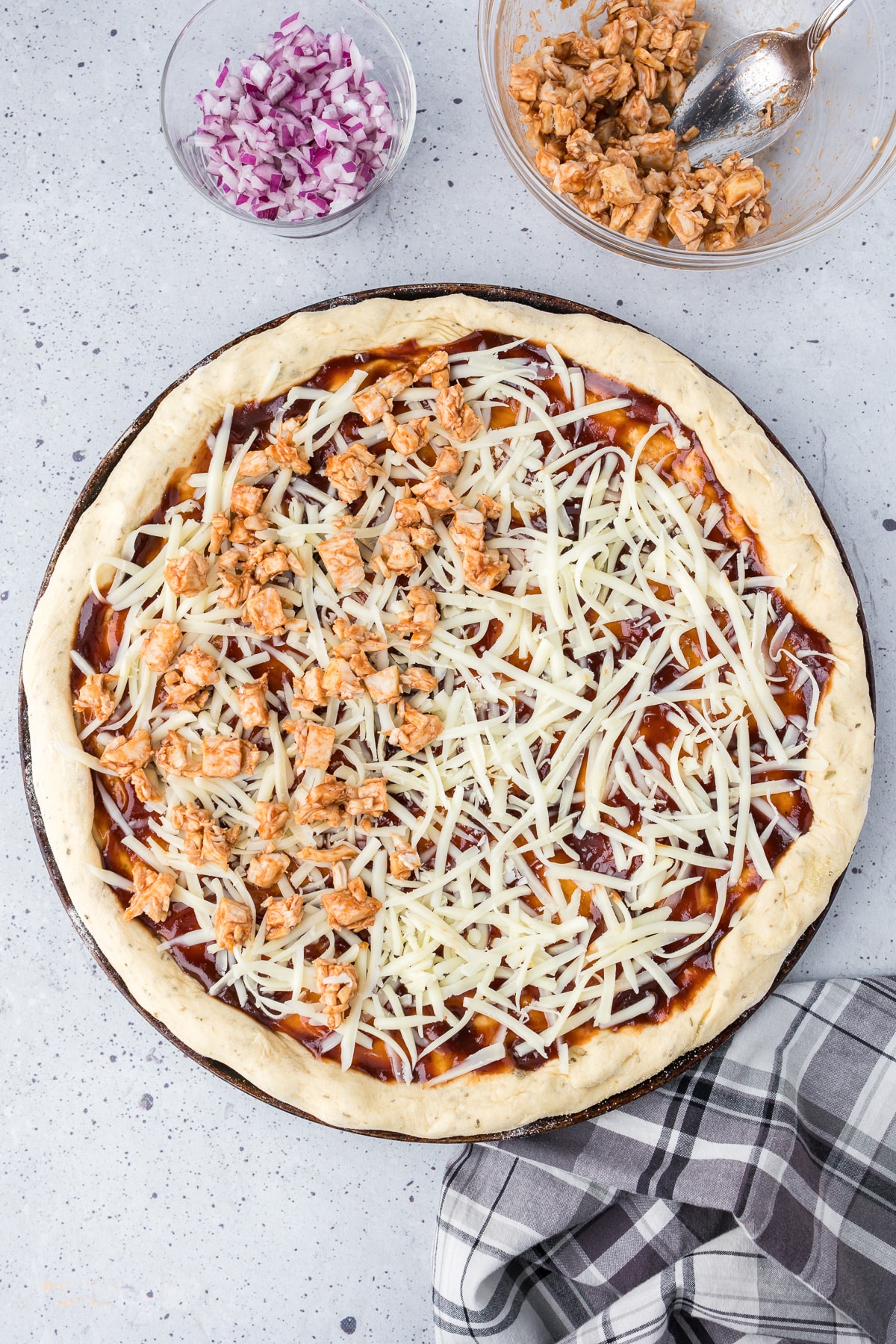 Chopped bbq chicken being spread over the top of pizza dough, sauce and cheese.