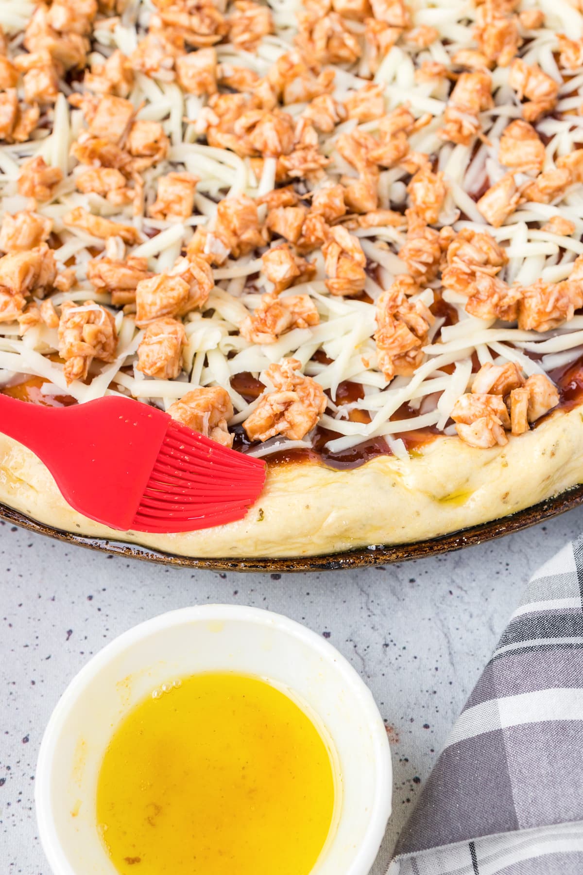 A bbq chicken pizza with a silicone brush adding olive oil to the dough on the edge.
