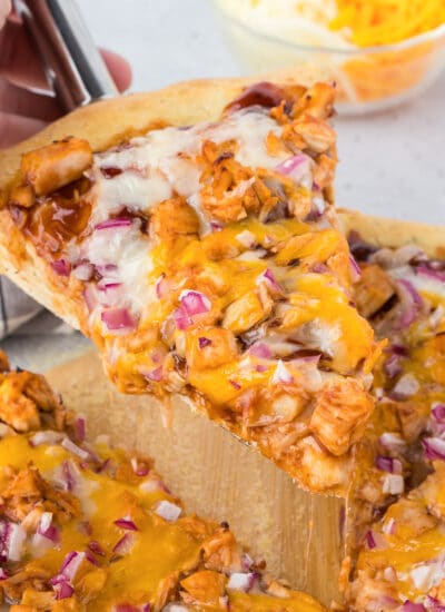 A slice of bbq chicken pizza on a wooden cutting board being lifted with a spatula.