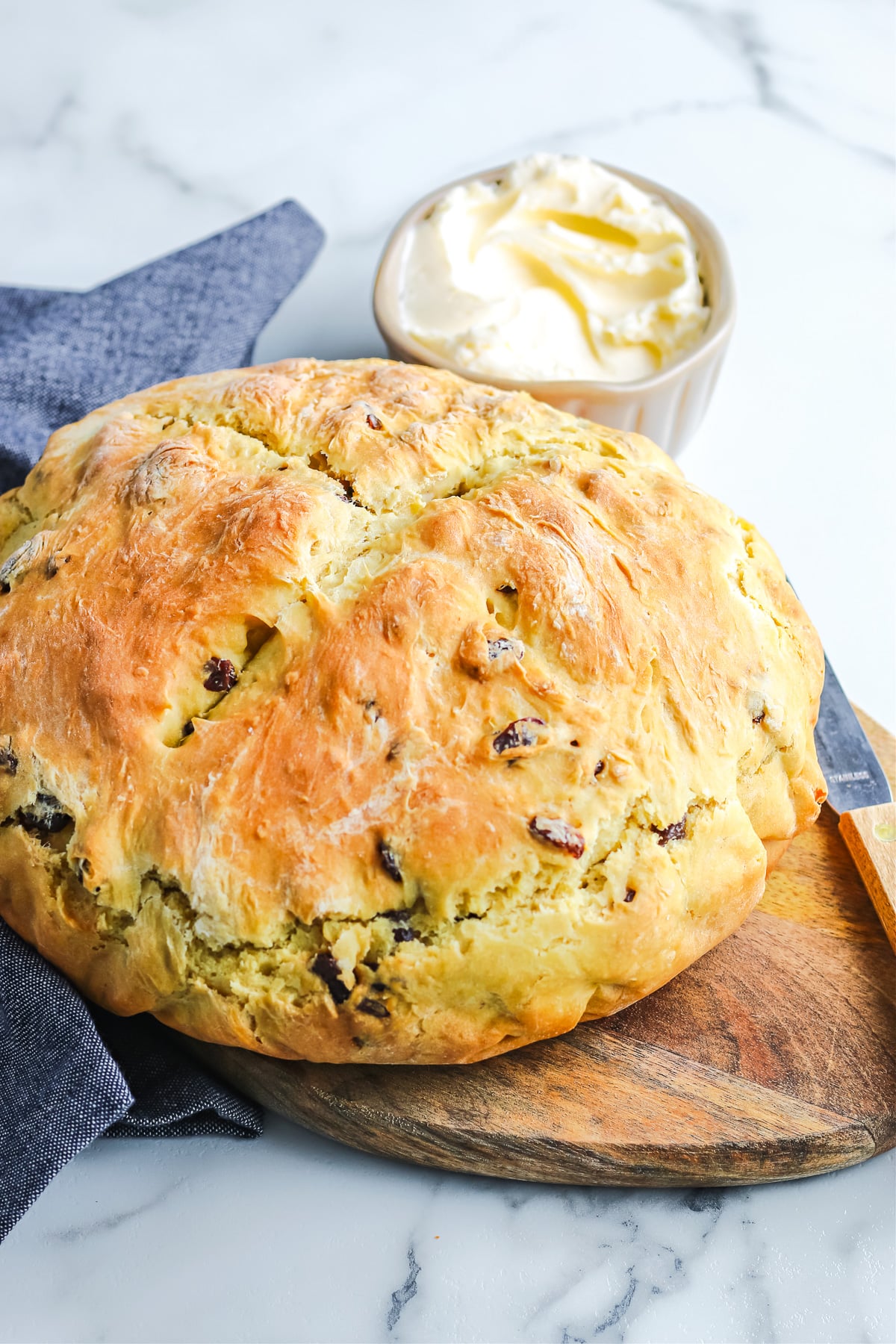 A loaf of Irish soda bread full of raisins sitting on a cutting board next to a small bowl of butter.