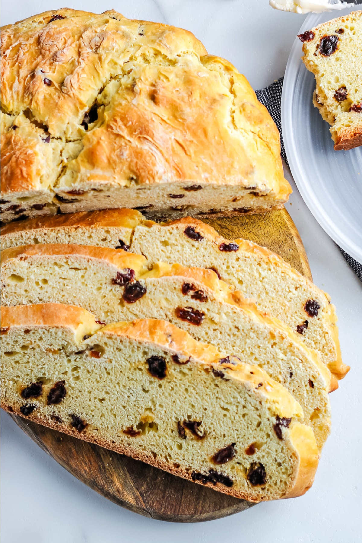 A loaf of Irish soda bread with raisins with three pieces of bread sliced to serve.