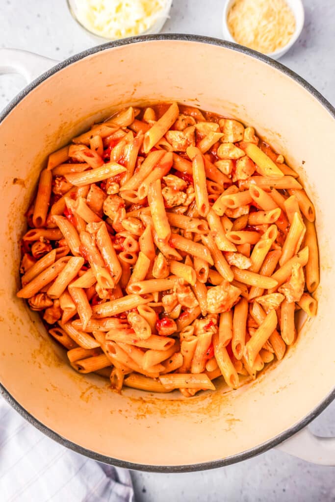 A pot of cooked penne pasta in red sauce with cooked chicken breast pieces in it.