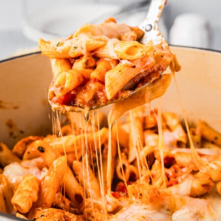 A spoon is being used to scoop a scoop of cheesy chicken parmesan pasta out of a pot.