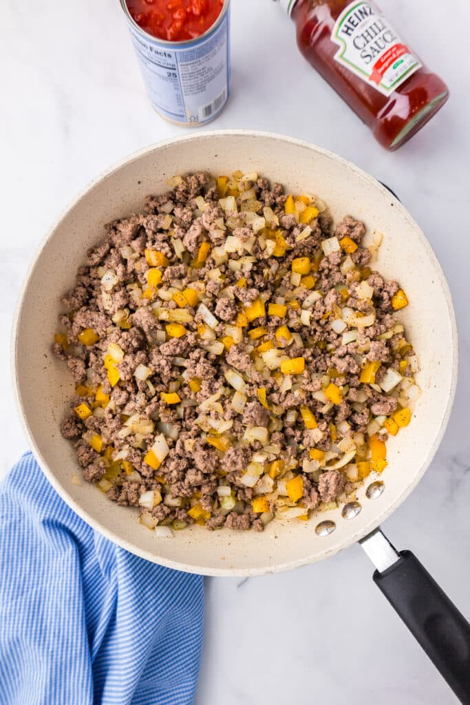 A frying pan with meat and vegetables next to a bottle of Heinz chili sauce and canned tomatoes for sloppy joes.