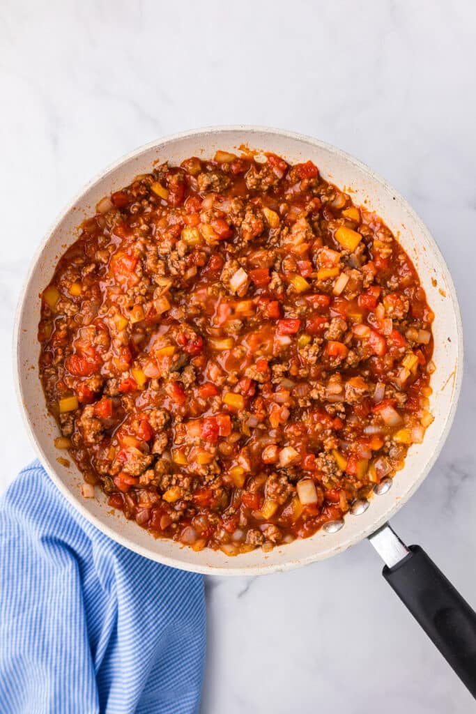 A skillet pan filled with ground meat, vegetables and tomatoes for sloppy joes.