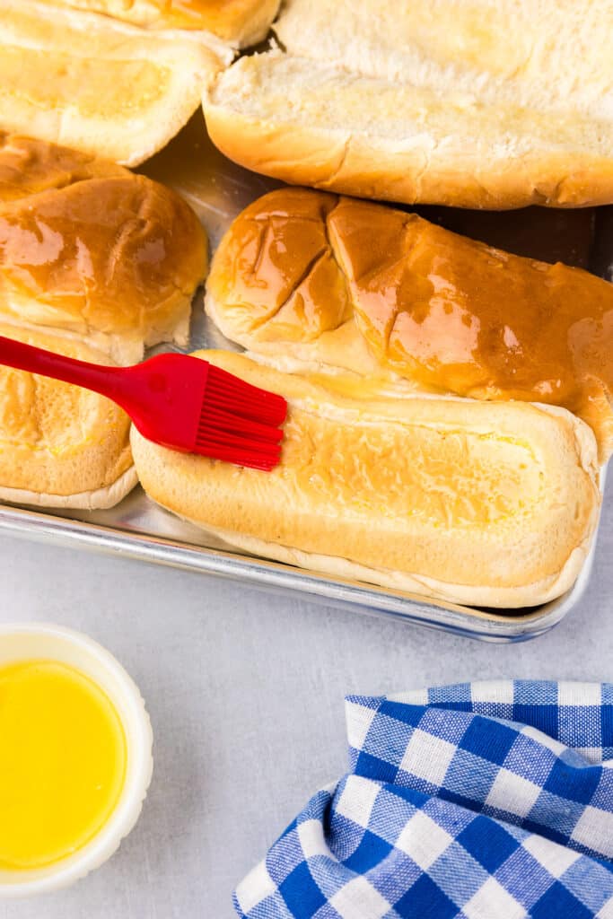 Buns on a pan being brushed with melted butter.