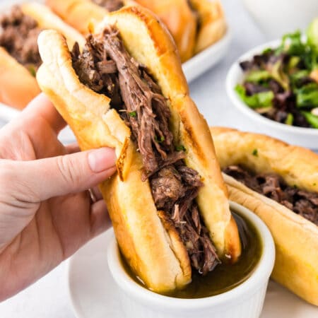 A person is holding a French dip sandwich with beef dipping it into an aus jus sauce.