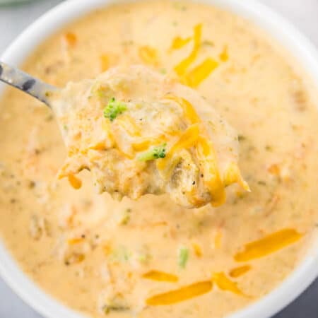 A bowl of broccoli and cheese soup with a spoon lifting a scoop of the soup up.