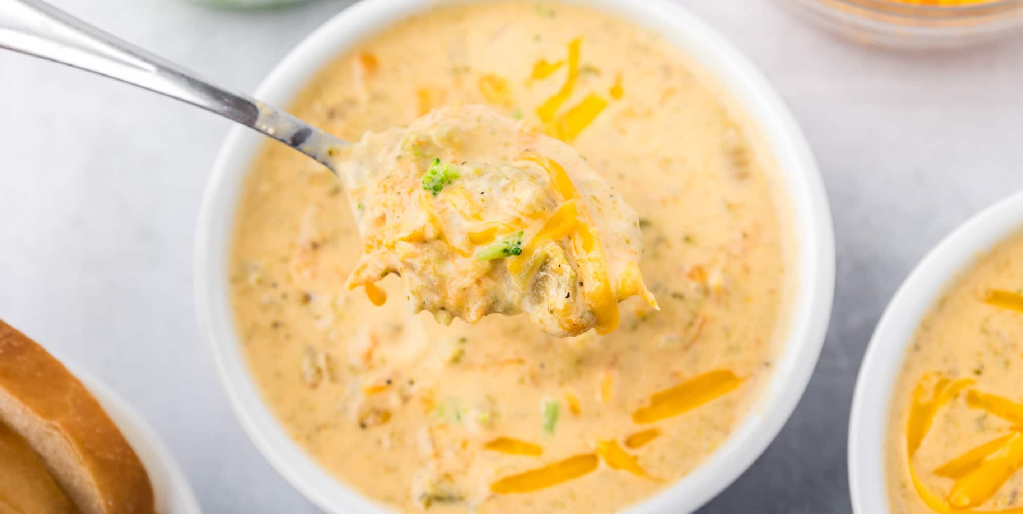 A bowl of broccoli and cheese soup with a spoon lifting a scoop of the soup up.