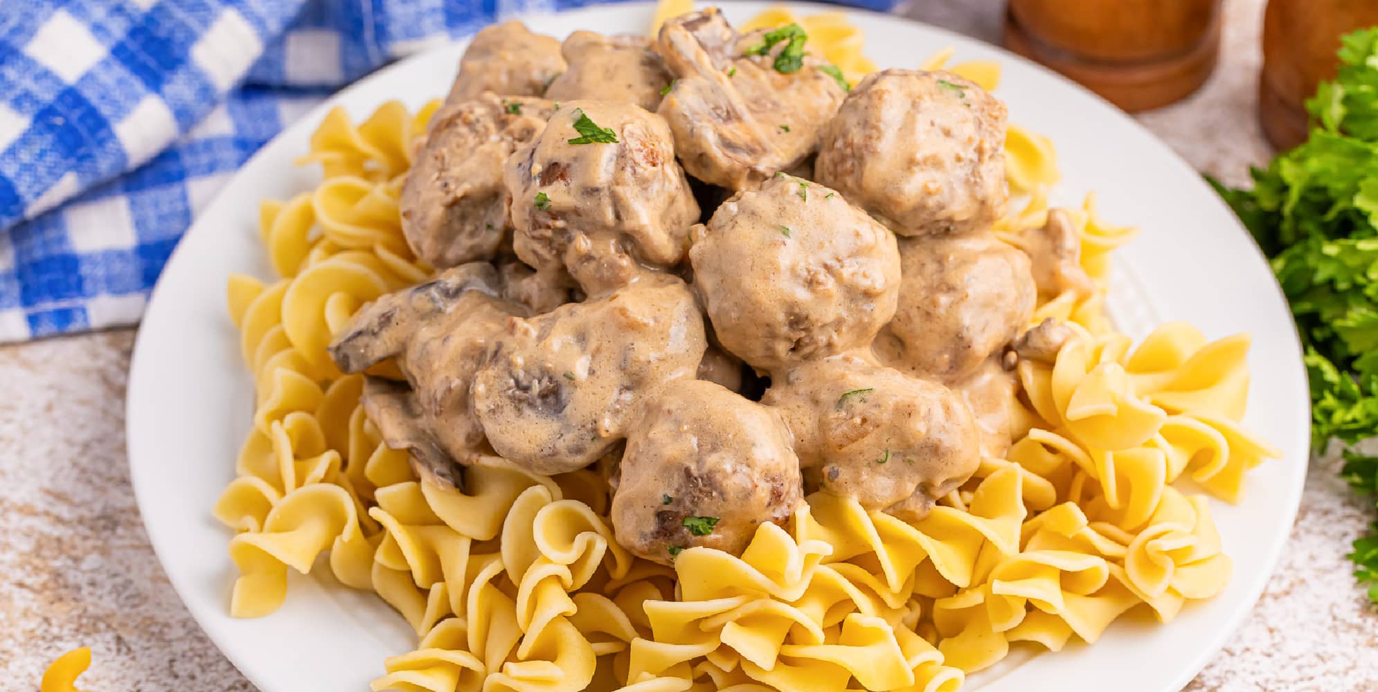 Wide view of meatballs stroganoff on top of egg noodles on a plate.