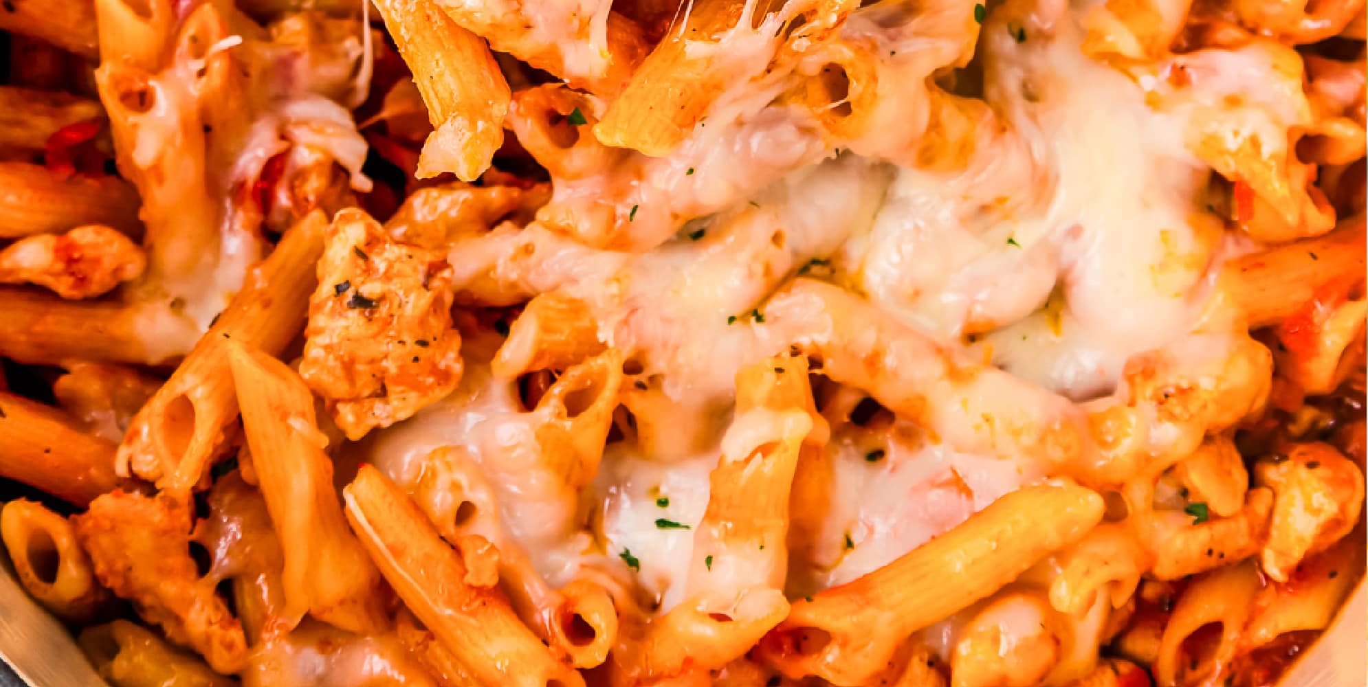 A close up of a dish of pasta with chicken and cheese.