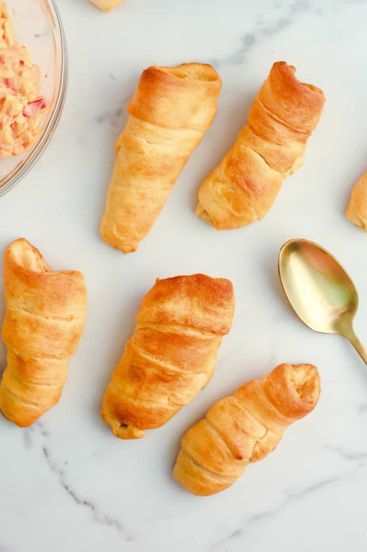 A plate of crescent roll cones with a bowl of pimento cheese dip and a spoon.