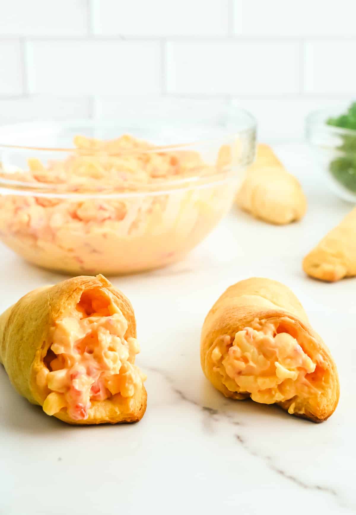 Crescent roll carrots from the end being stuffed with pimento cheese with a bowl of pimento cheese in the background.