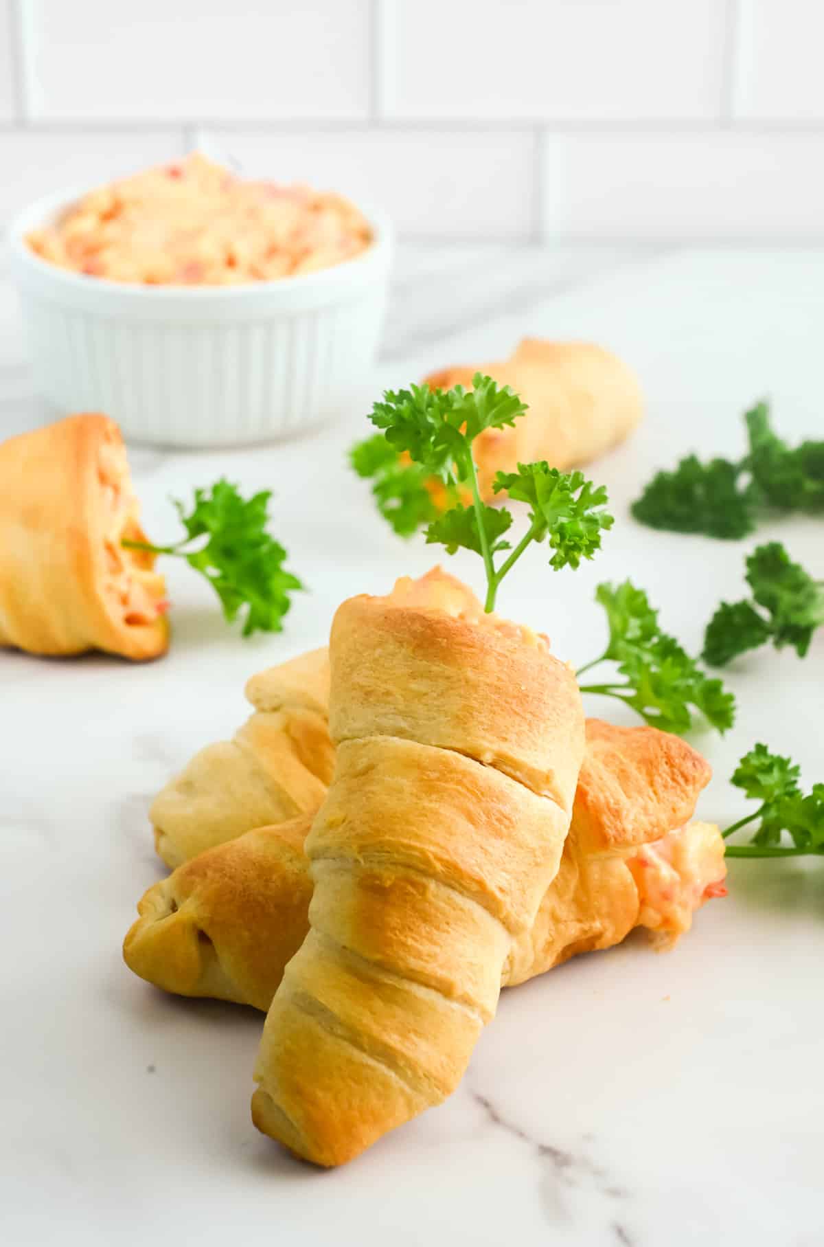Cheesy crescent rolls with parsley shaped like carrots on a marble counter.