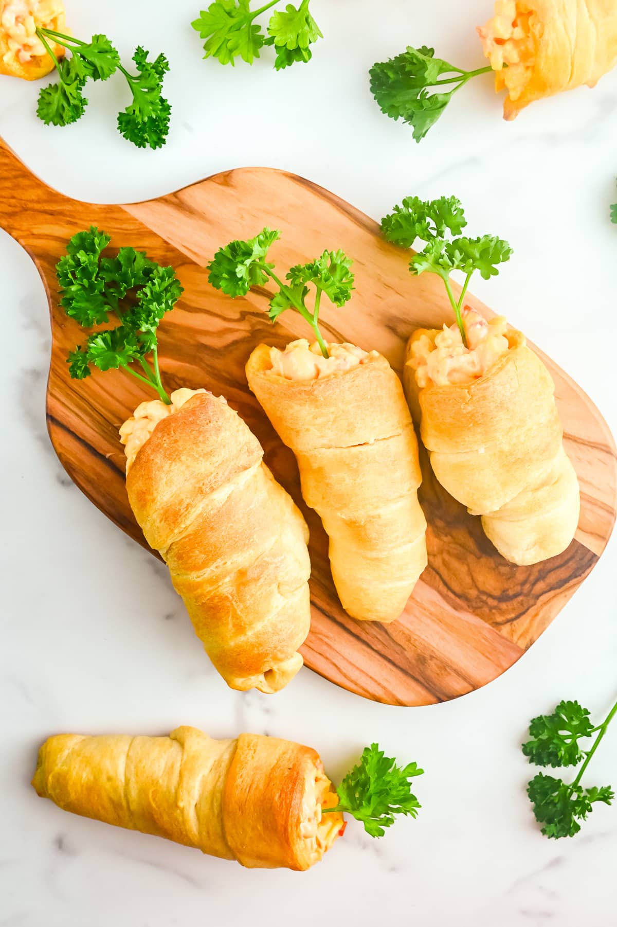 Carrot shaped stuffed crescent rolls on a serving board with parsley carrot tops.