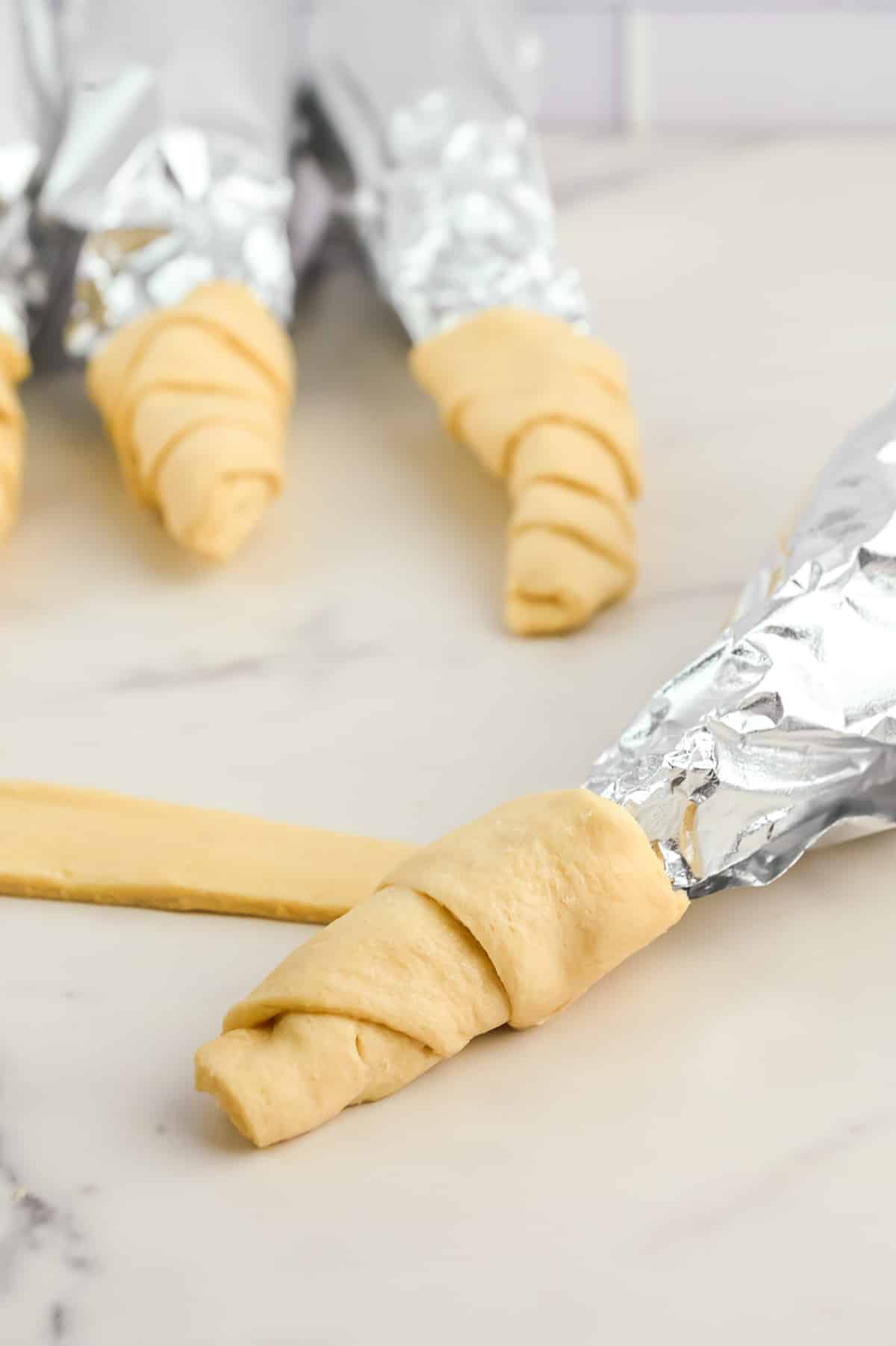 Crescent roll dough being wrapped around a piece of foil on a counter.