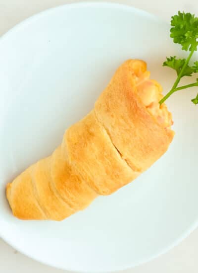 A carrot shaped crescent roll with a parsley as a carrot top on a plate.