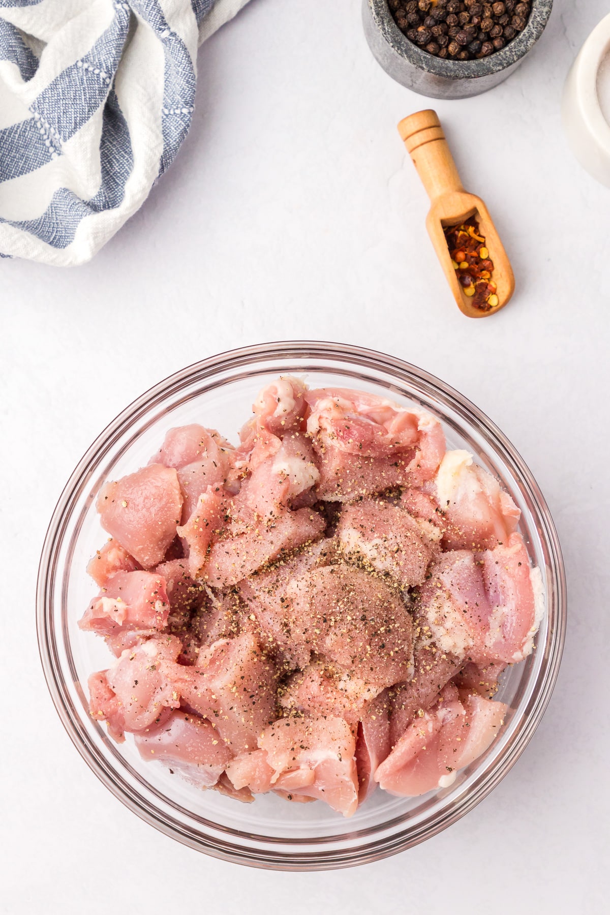 Chopped raw chicken thighs in a glass bowl for creamy chicken and rice seasoned with salt and pepper.