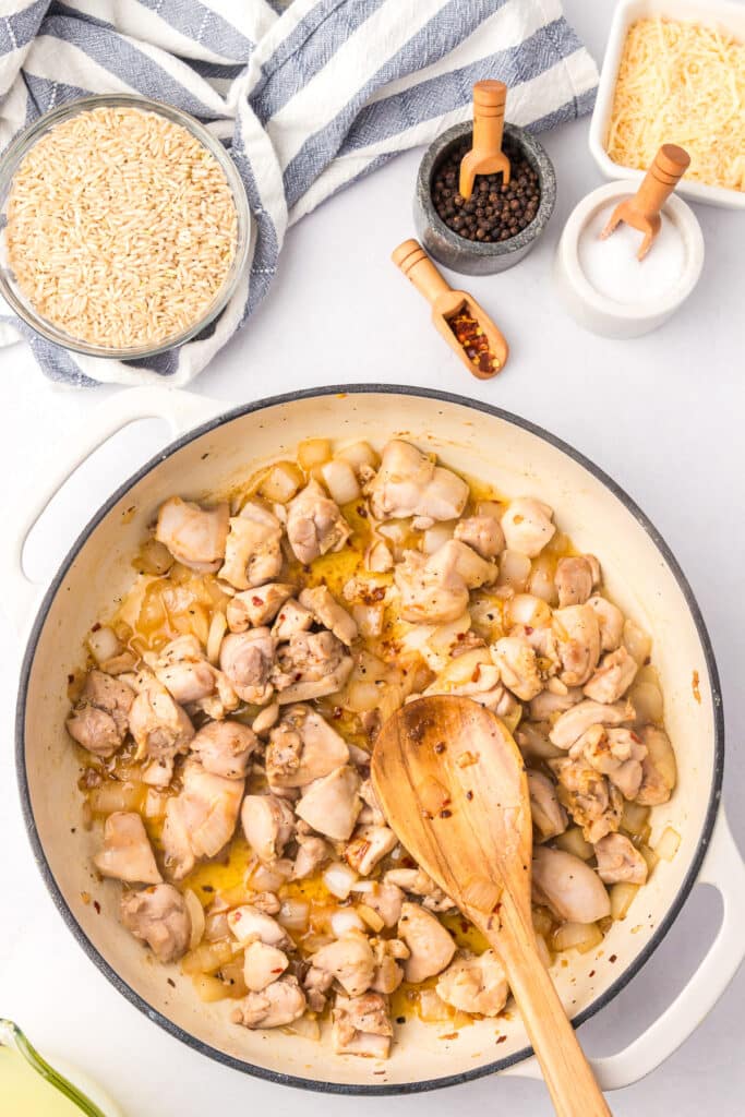 Cooked chicken thigh in a pan with spices and a wooden spoon to make creamy chicken and rice.