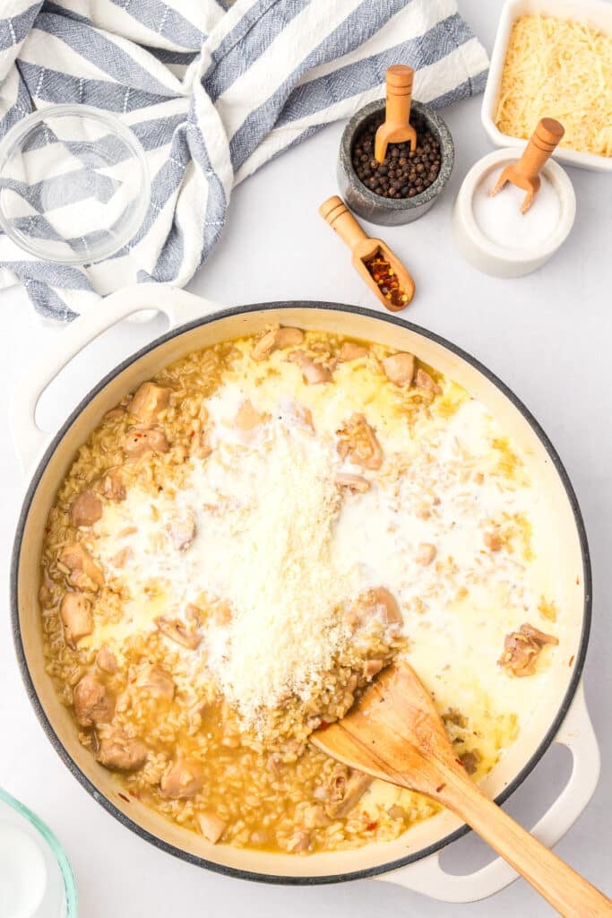 Stirring cream and parmesan cheese into chicken and rice in a pan with a wooden spoon.