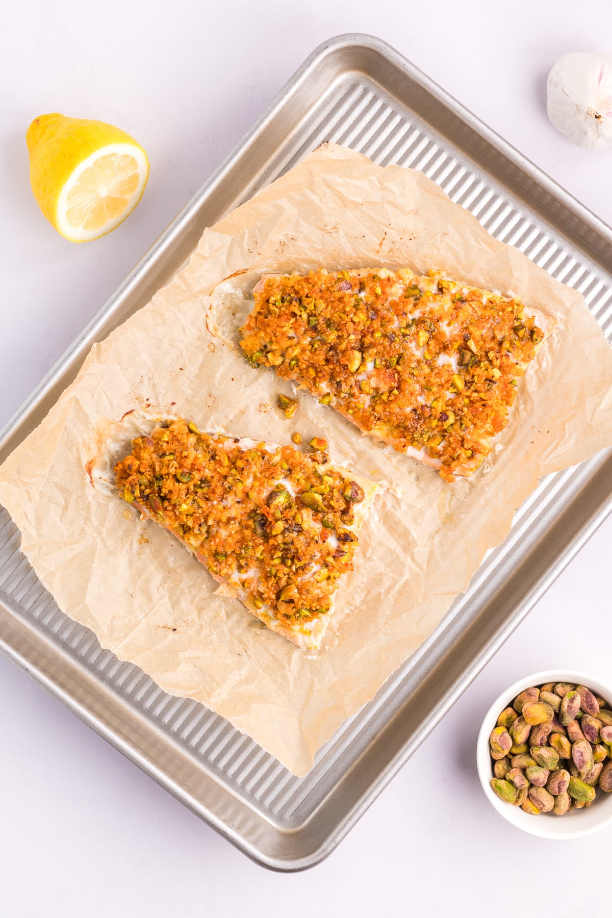 Two salmon fillets on a baking sheet with a pistachio after baking.