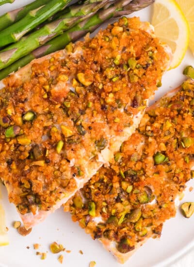 Pistachio crusted salmon on a plate with asparagus and lemon on a table.